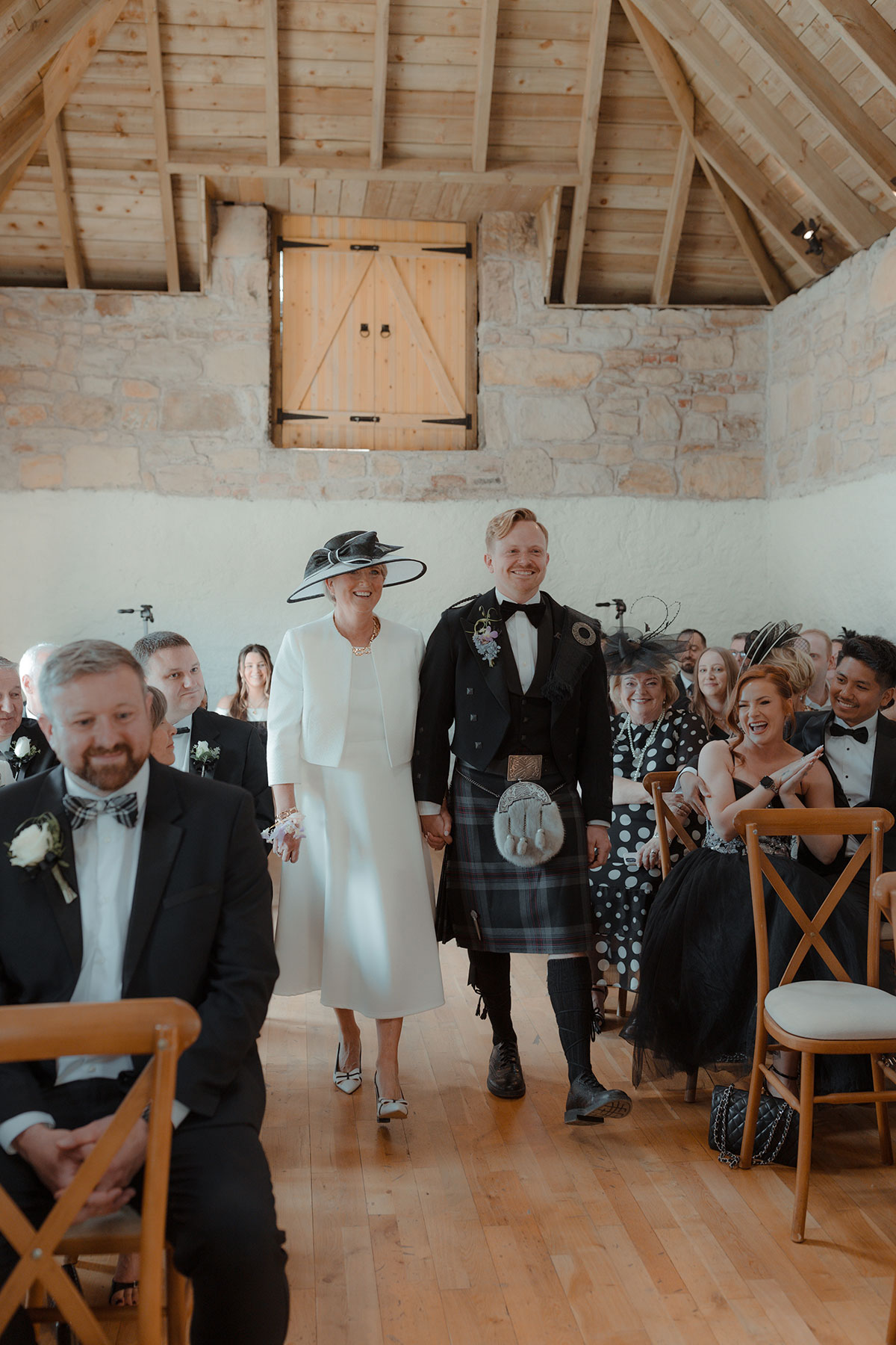 Groom holding hands with his mum as they enter barn ceremony space at Falkirk farm wedding