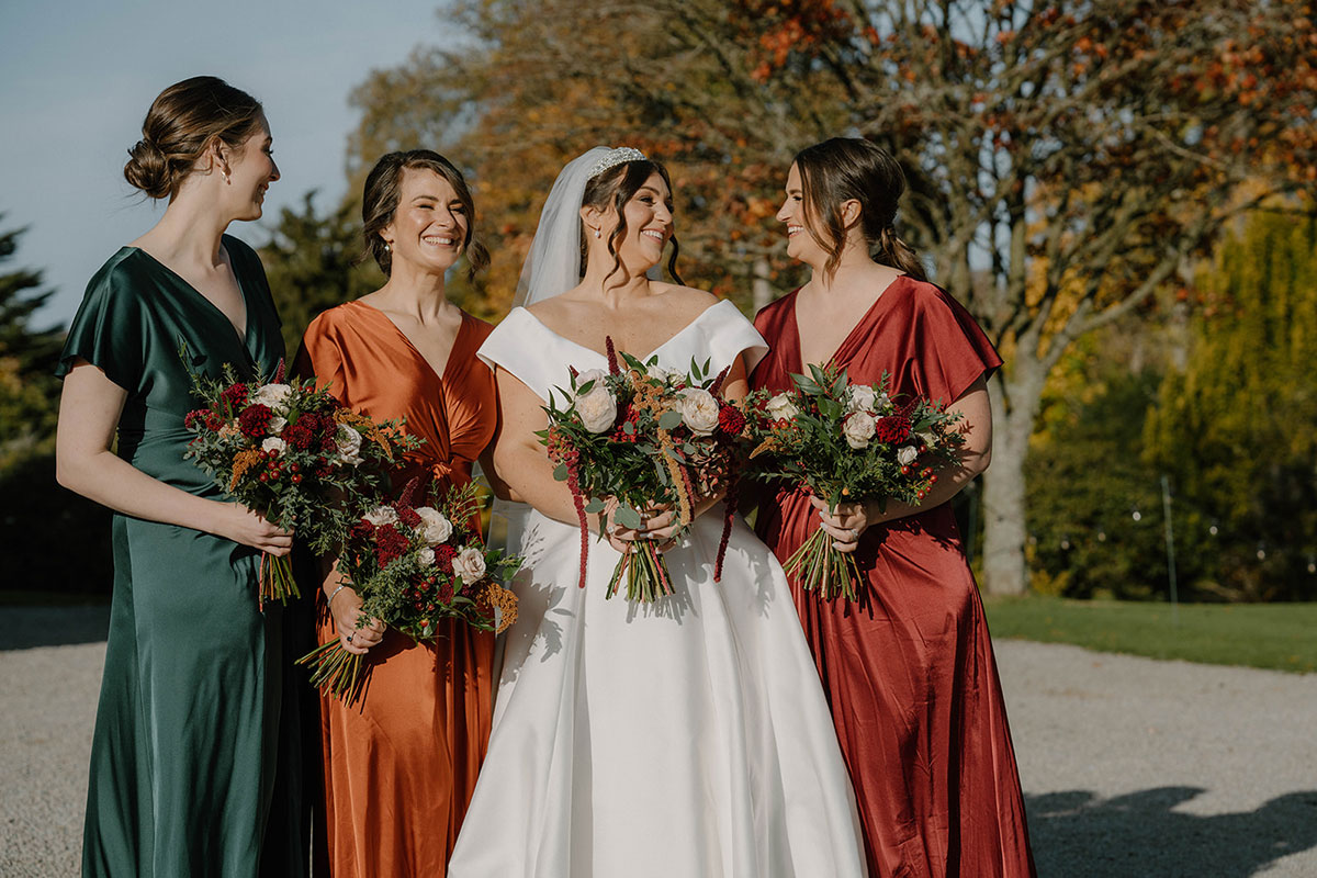 A bride standing with her bridesmaids, all in different coloured dresses