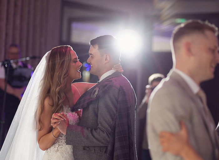 a bride and groom dancing in an atmospheric darkened room with bright light in background