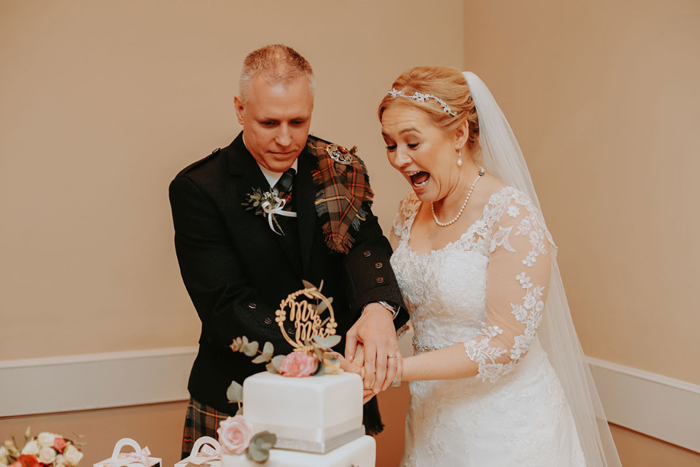 Bride looks excited as she cuts wedding cake with groom 