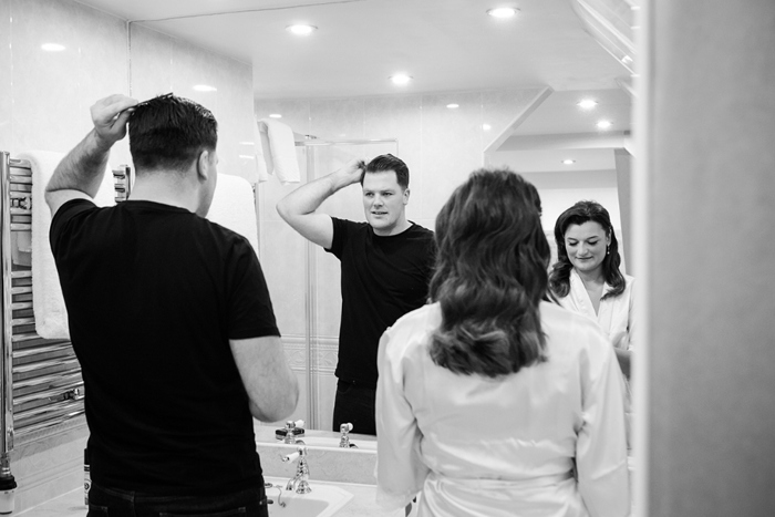 Black and white photo of the bride and groom getting ready in front of the mirror