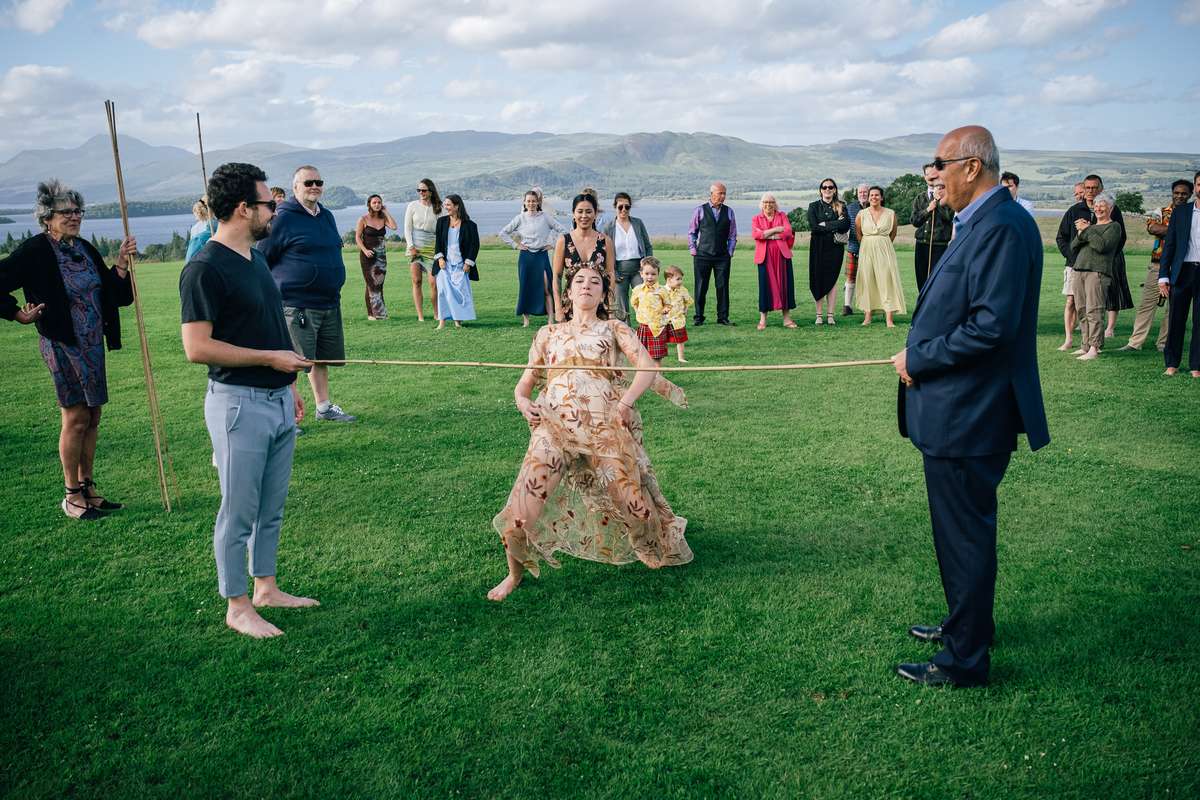 Wedding guests playing limbo on the lawn at Ardoch Loch Lomond with mountain views behind