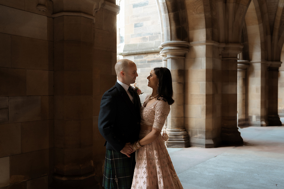 A Bride Wearing A Pink Lehenga And Groom Wearing A Kilt Dancing In The Cloisters At Glasgow University