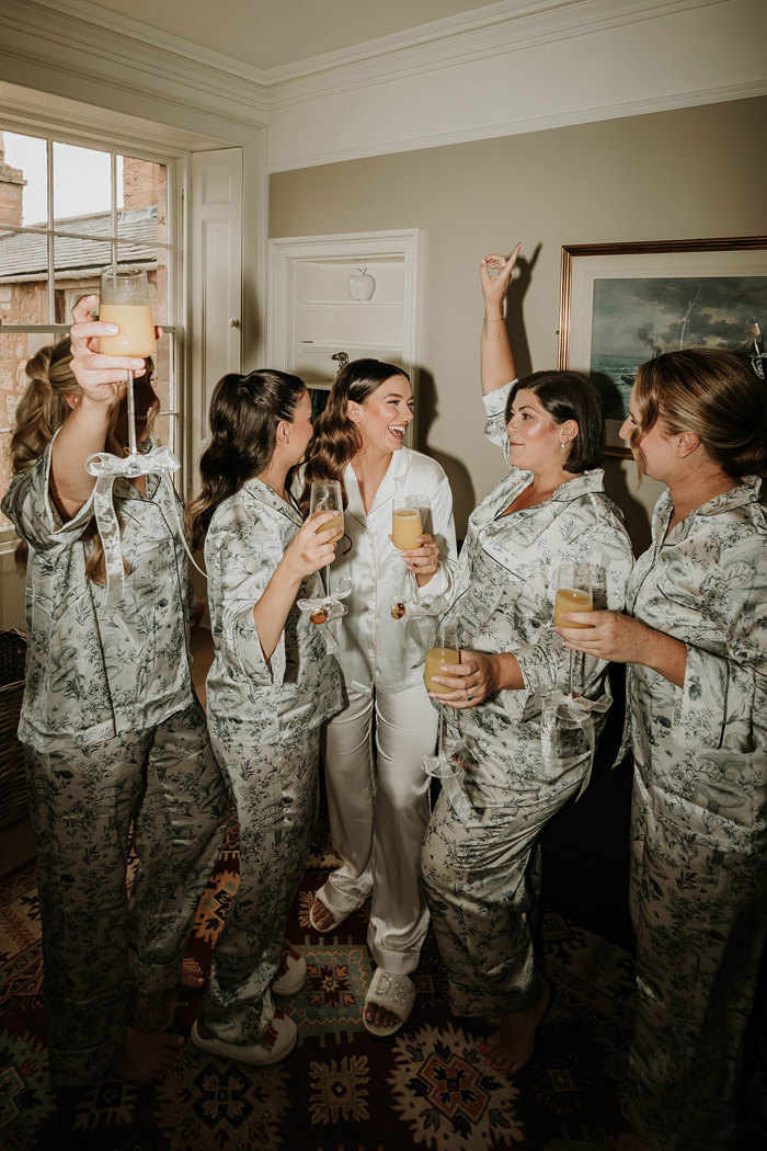 a bride and group of bridesmaids wearing silky pyjamas and drinking mimosas 