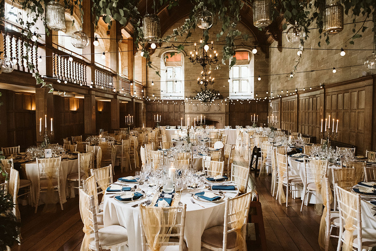 Grand ballroom reception setup at Achnagairn Castle with round tables, candlelit décor and hanging greenery in the vaulted hall