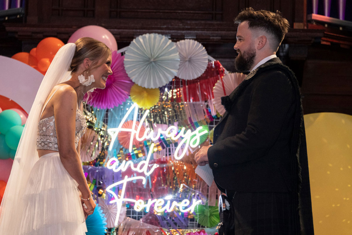 Neon sign reads 'Always and Forever' behind bride and groom during their ceremony