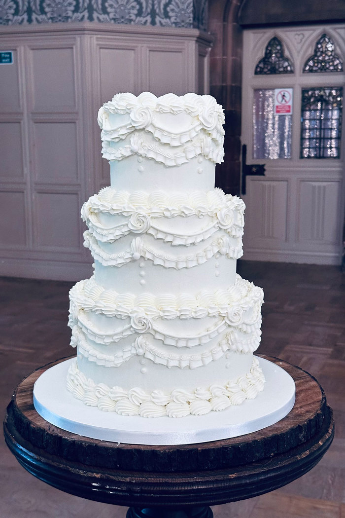 three-tier white wedding cake decorated with vintage buttercream style icing in ribbons and roses