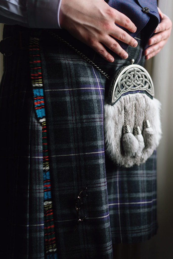 close up image of a tartan kilt, grey sporran and kilt pin on a groom