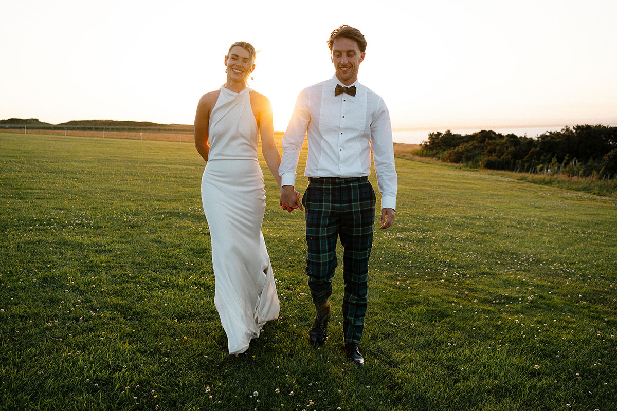 Bride and groom walking at sunset near Kinkell Byre in St Andrews during colourful Scottish wedding.