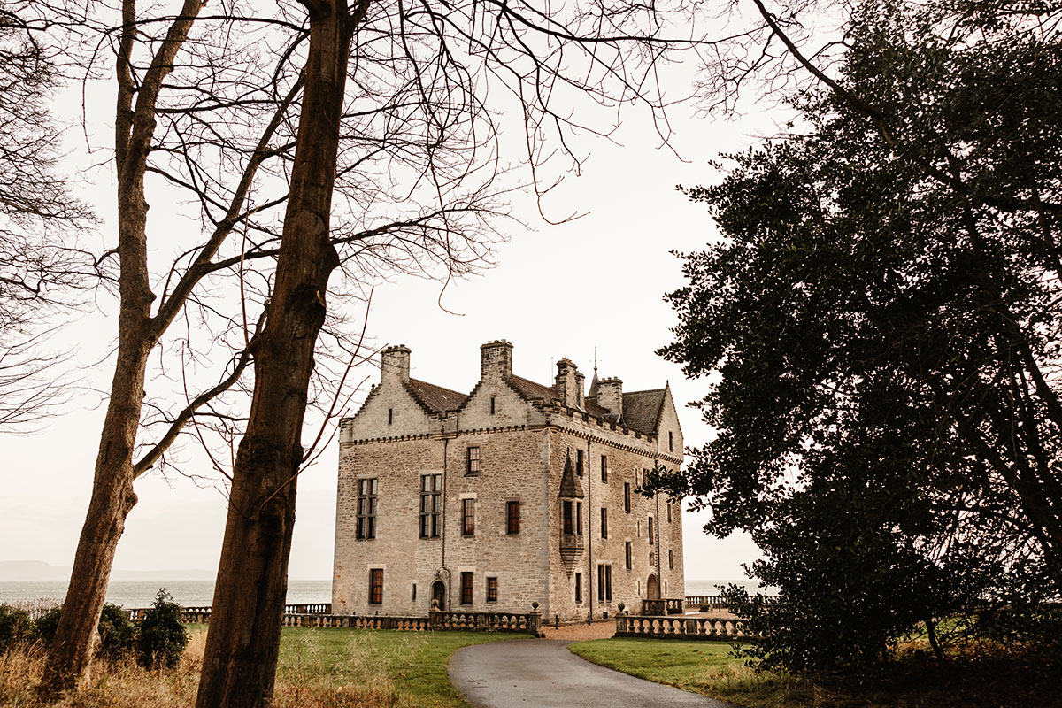 Stone exterior of Barnbougle Castle framed by winter trees, overlooking the water.