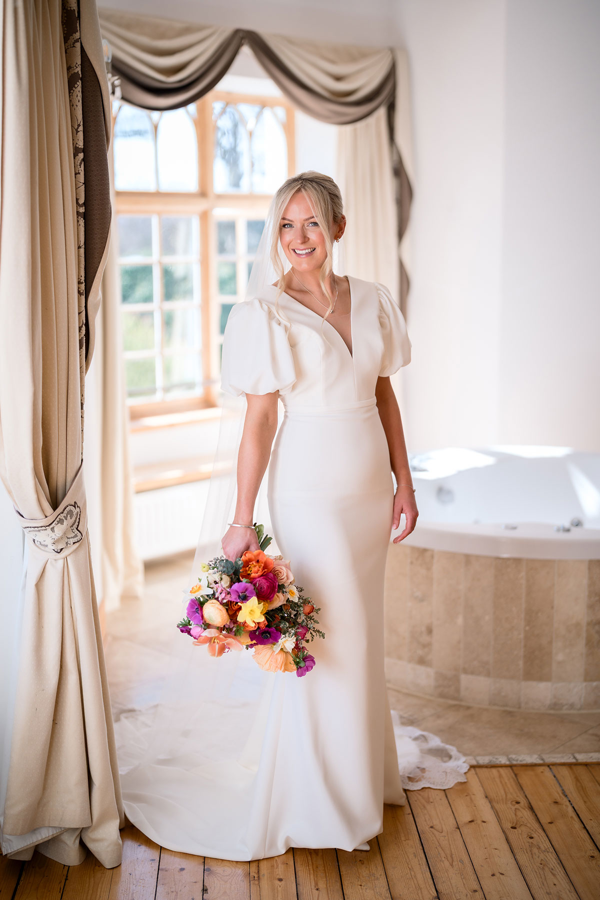 bride wearing a fitted wedding gown and puff sleeves holds a colourful bouquet at achnagairn castle