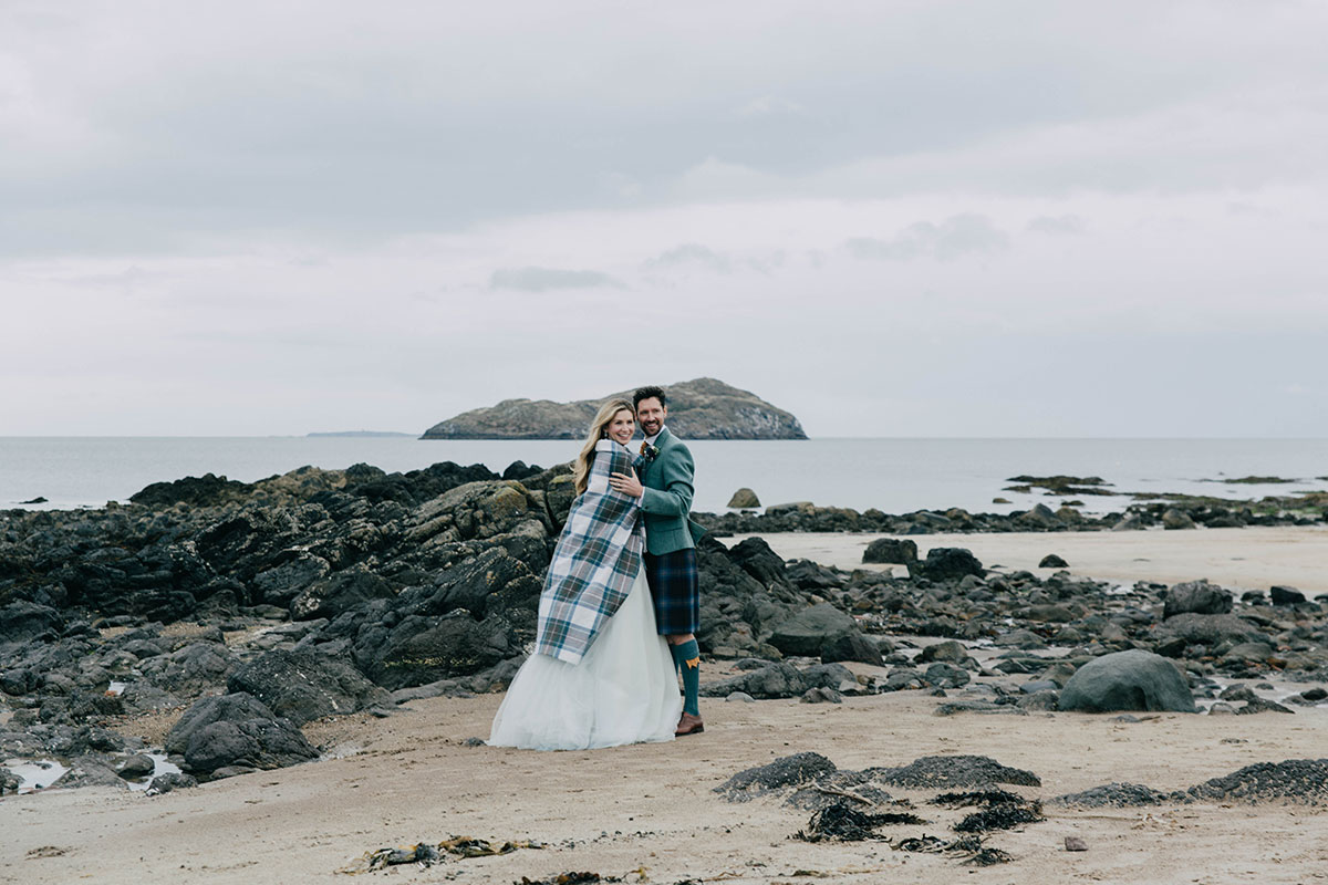 Bride and groom wrapped in a tartan blanket for wedding photos on North Berwick beach, Scotland