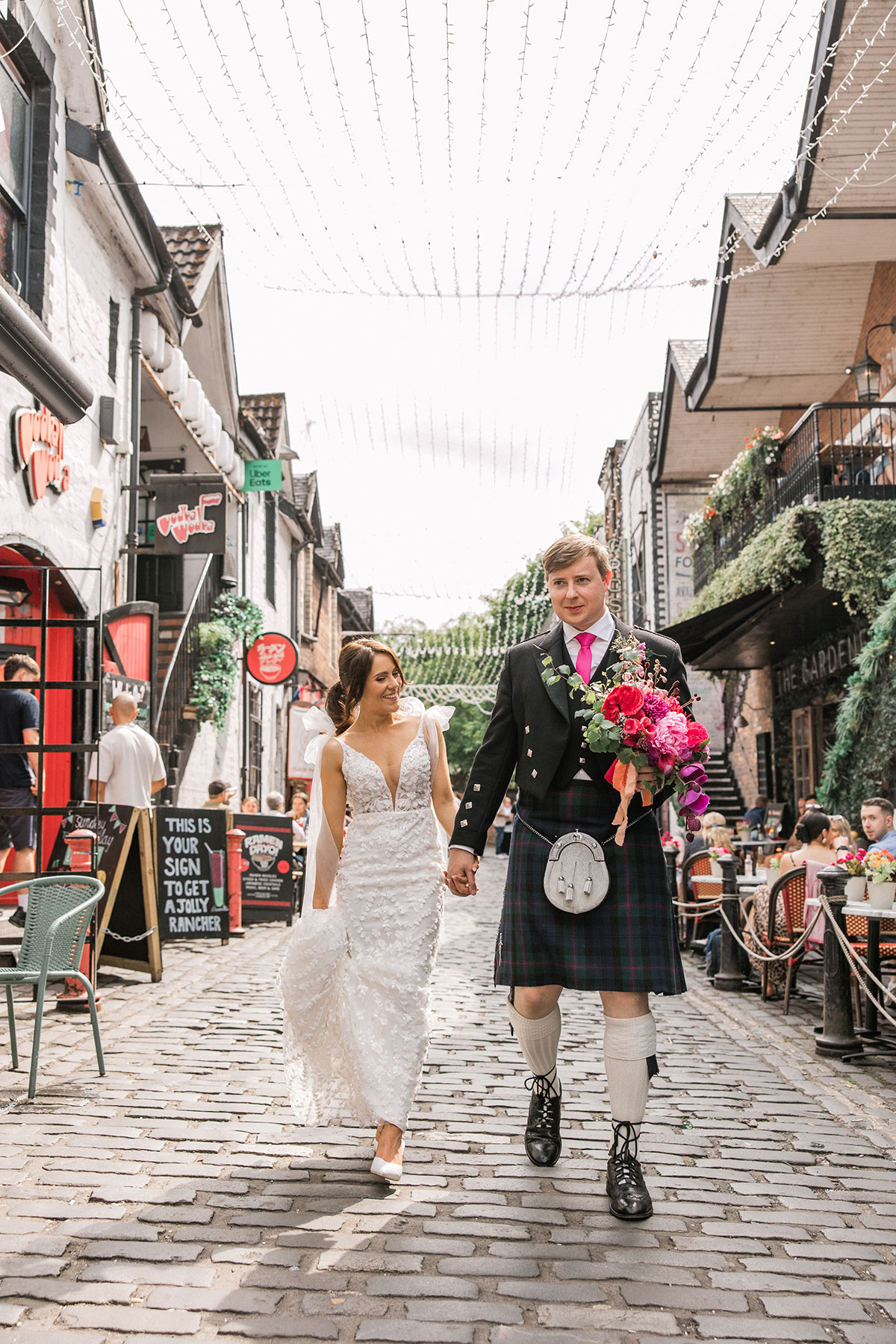 Bride and groom walking hand in hand along a cobbled city street after their wedding ceremony