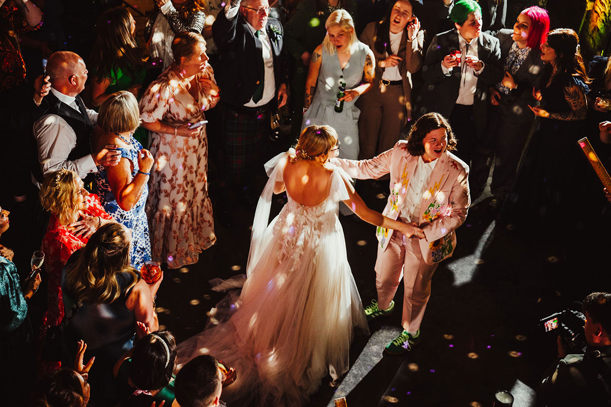 Aerial view of the brides dancing together on a crowded Engine Works dancefloor lit with disco lights and surrounded by guests.