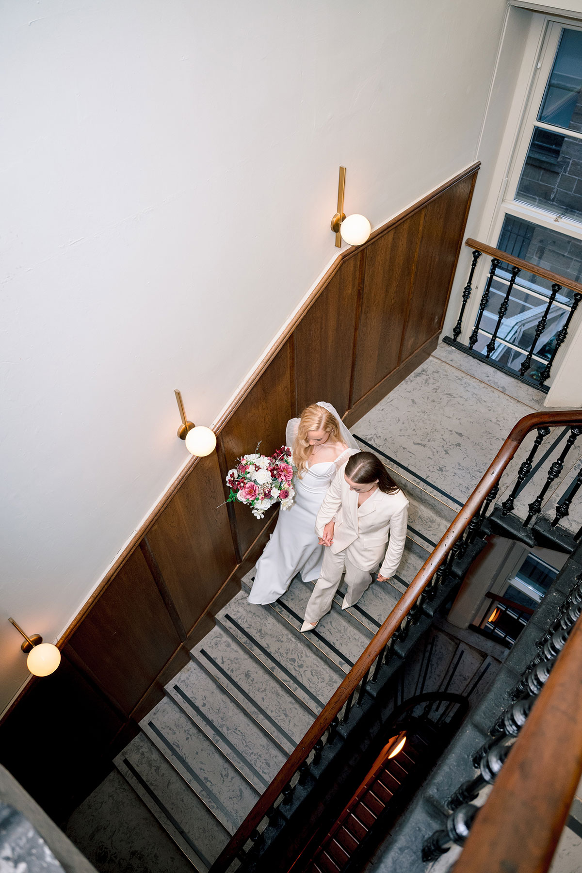 Two brides walking down staircase at The Exchange Glasgow, dress and suit.