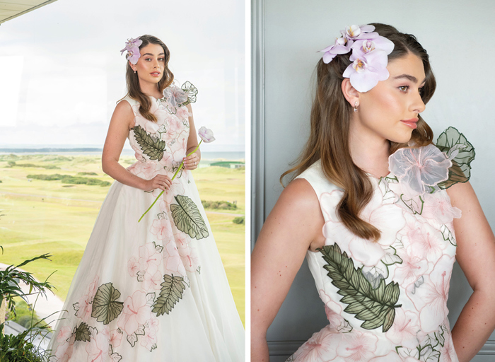 A woman in a long white dress with pink flower and green leaf applique over the dress and pink orchids in her hair