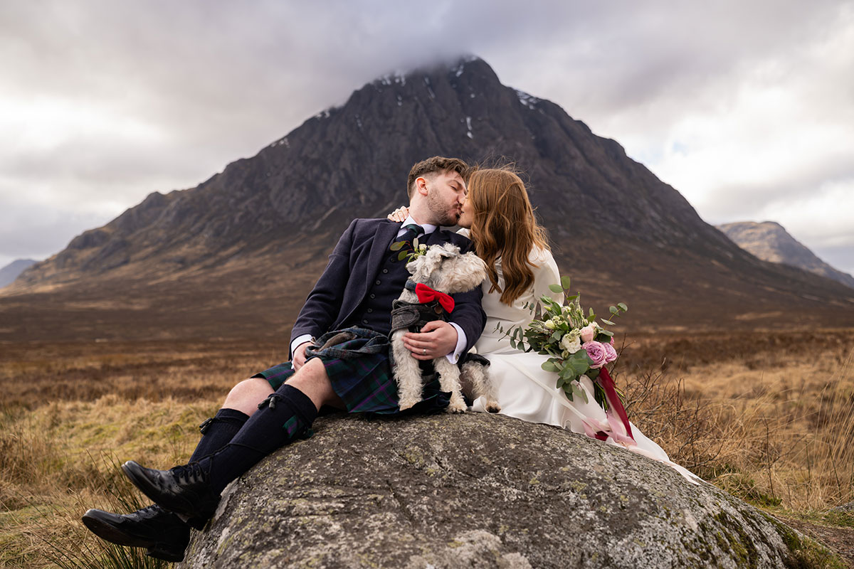 Bride and groom sharing a kiss with their schnauzer dog in front of Buachaille Etive Mòr during a Glencoe elopement photoshoot