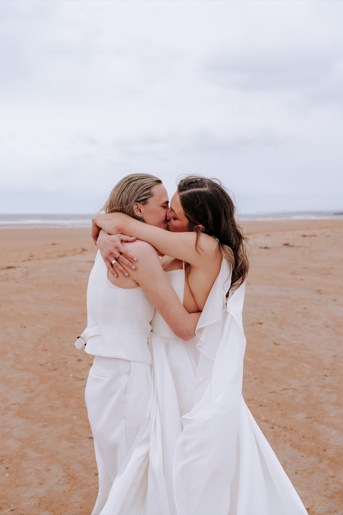 Hannah and Donna kissing and embracing during their wedding portraits on the beach.