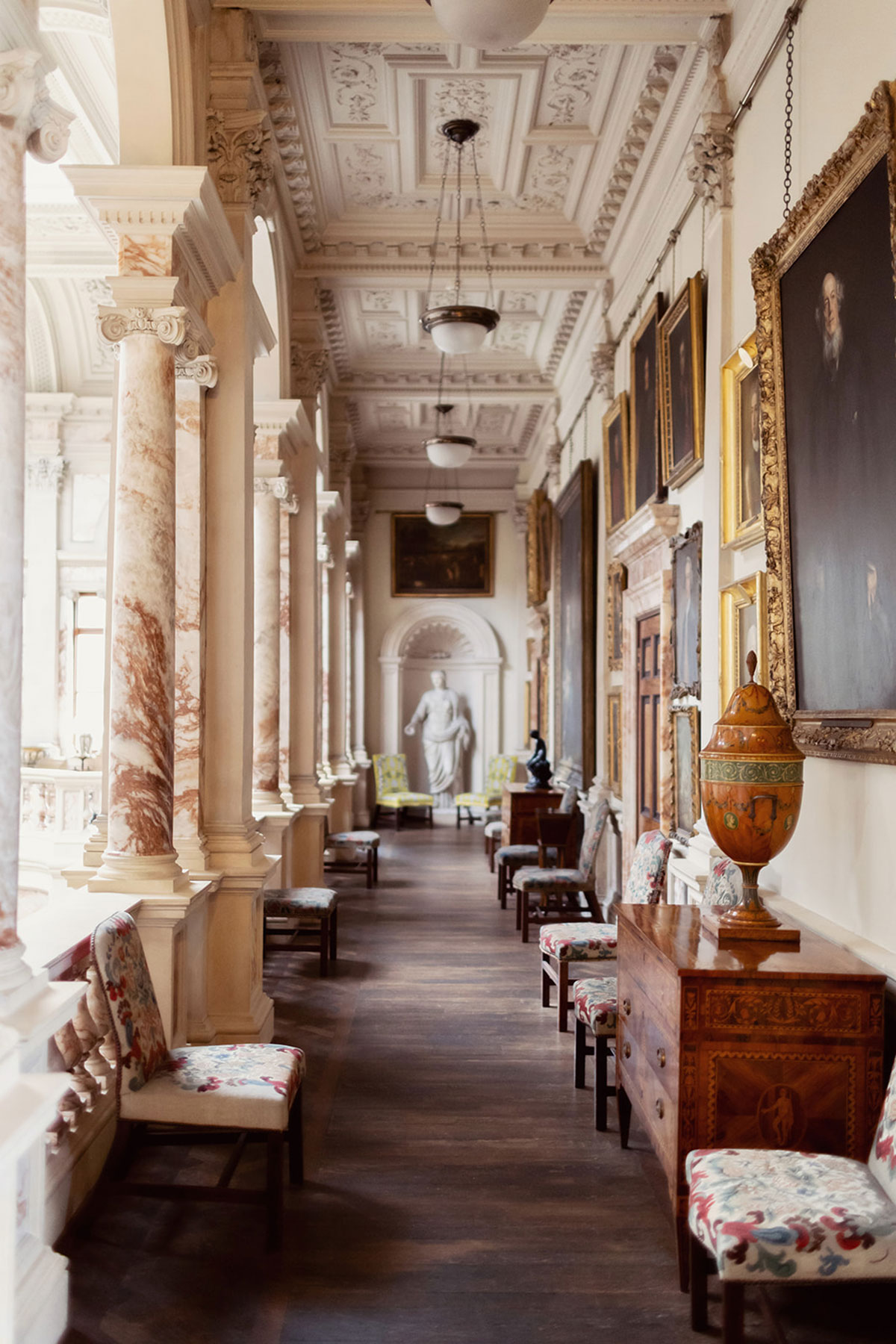 Grand corridor at Gosford House with marble columns, framed portraits and period furniture.