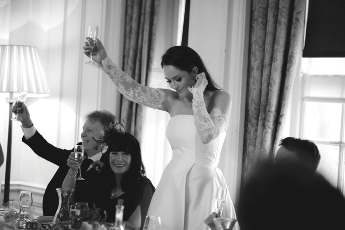 A Person Wearing A Wedding Dress Raising A Champagne Glass To Toast
