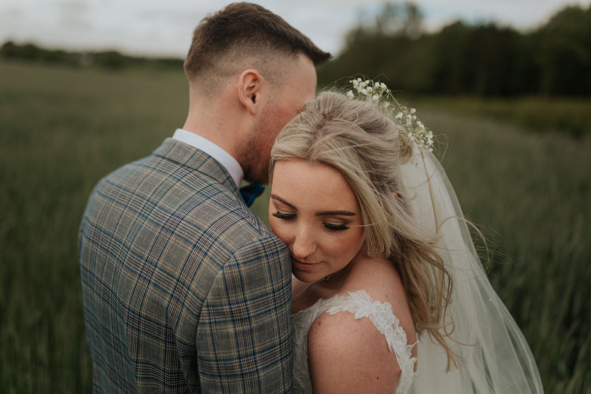 A close up of faces of a Bride And Groom Posing For A Wedding Photo In A Field Of Tall Grass
