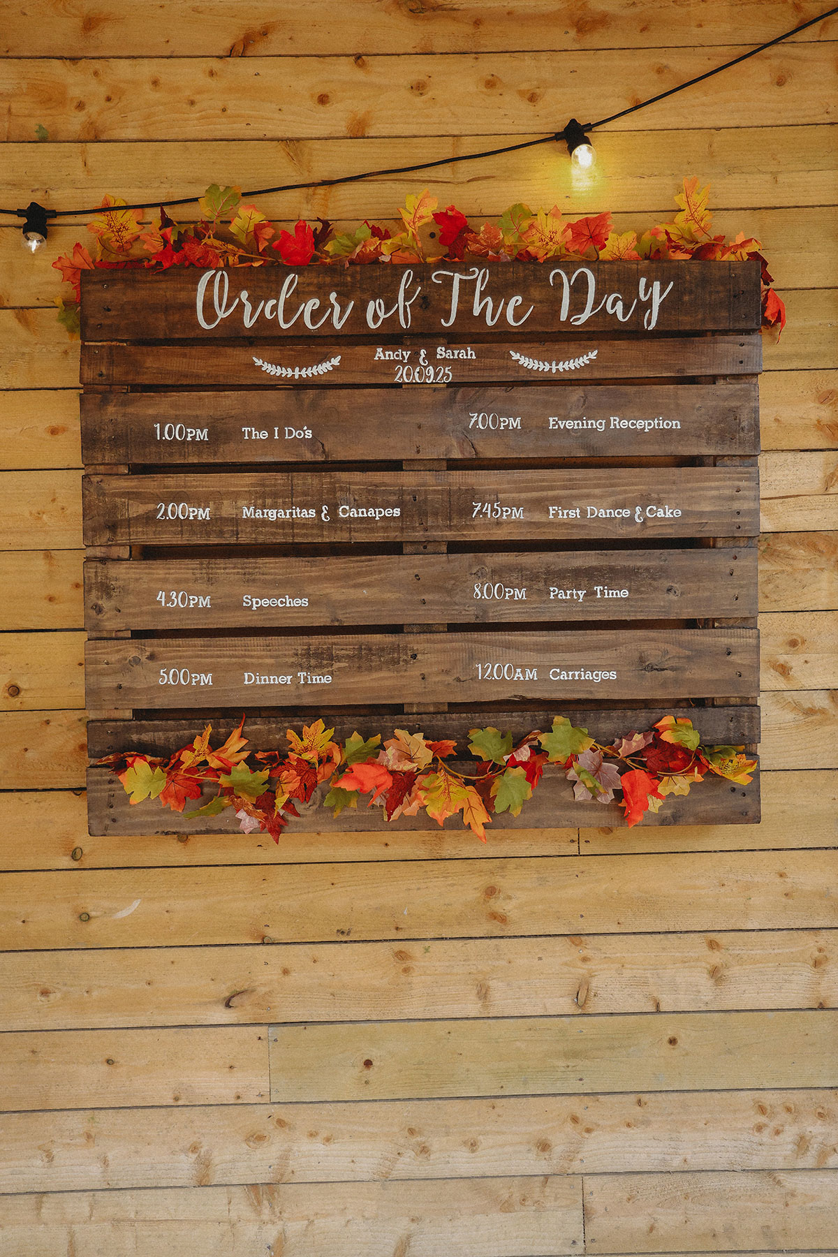 Rustic wooden order of the day wedding sign decorated with autumn leaves at an outdoor Scottish wedding venue