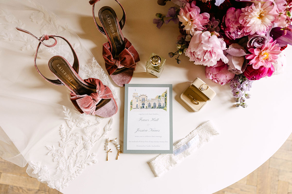 Wedding invitation flat lay with pink shoes, rings, perfume, jewellery and bouquet at Drumtochty Castle wedding