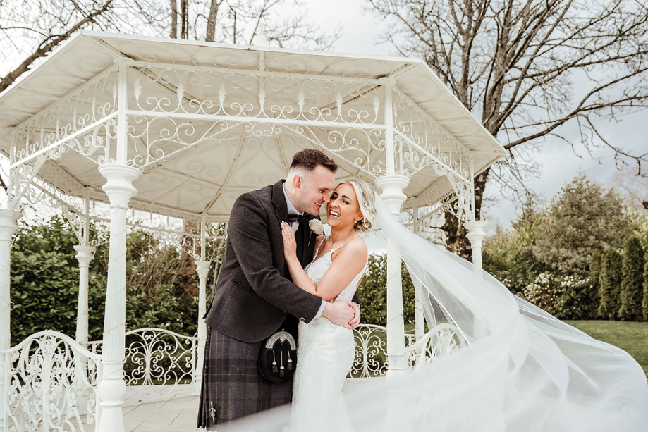 a bride and groom embrace with the bride's veil floating behind her