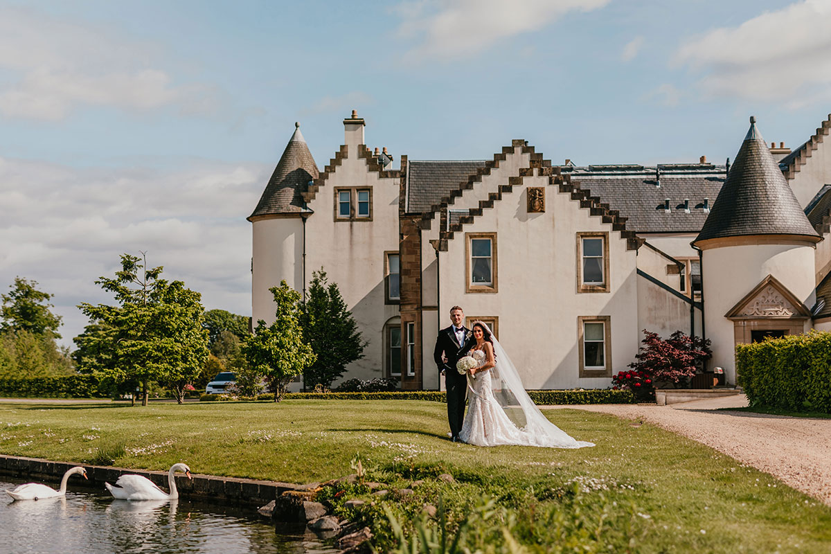 bride and groom stand on green grass in front of ingliston country club on wedding day
