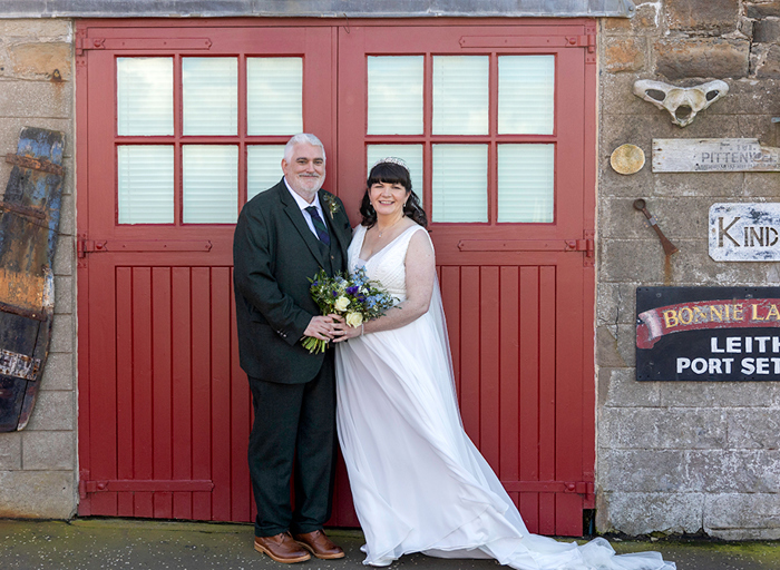 a bride and groom posing in front of red painted doors on a boat house