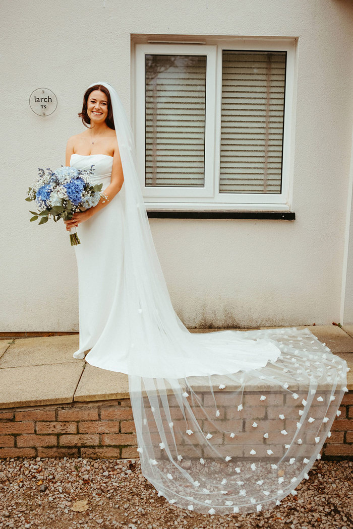 full length picture of bride wearing floral veil and holding blue flowers