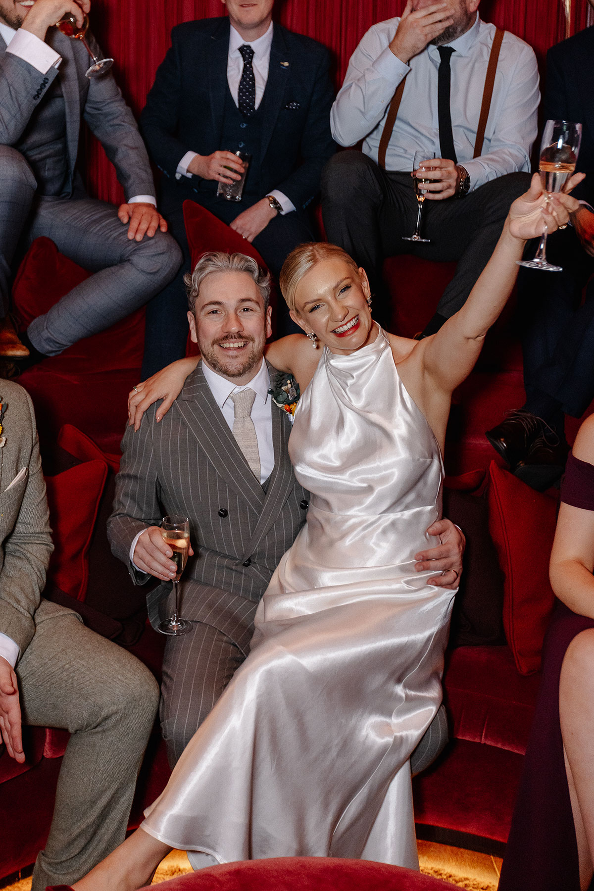 Wedding guests celebrate with the couple inside the Scarlet Lounge at Virgin Hotels Edinburgh, surrounded by dramatic red décor and statement lighting.