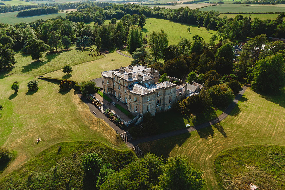 Drone shot of Newton Don House surrounded by expansive lawns, mature woodland and open countryside in the Scottish Borders.