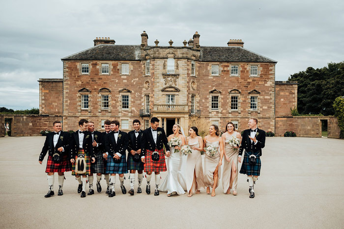 A group of people wearing wedding attire walking in front of Archerfield House.