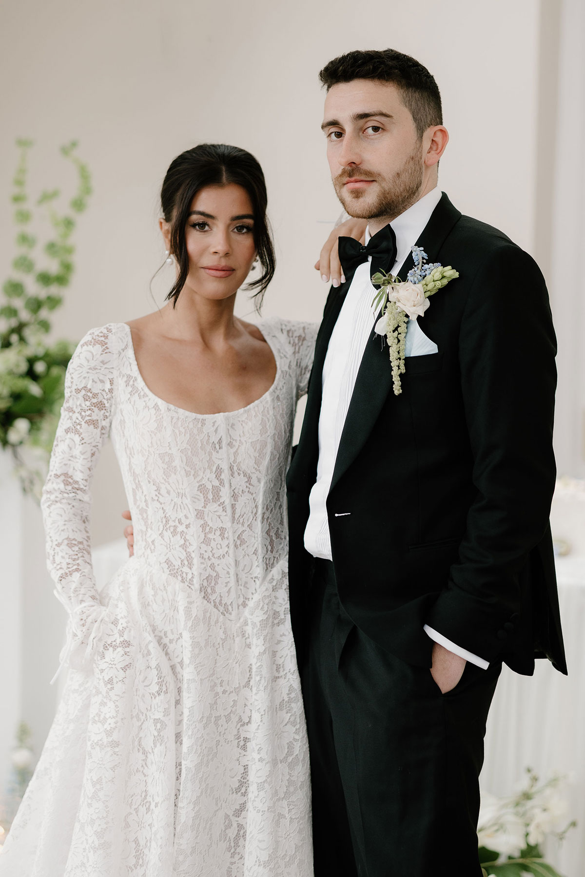 Bride in a long-sleeved lace wedding dress standing beside a groom in a black tuxedo