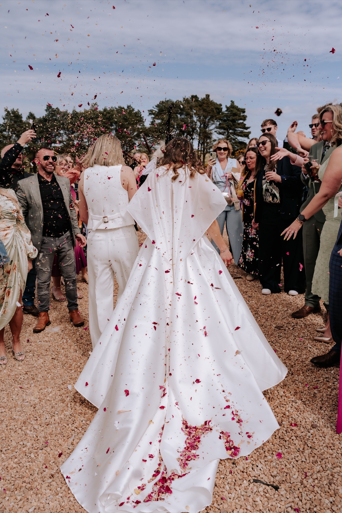 Hannah and Donna walking through a shower of colourful flower-petal confetti at their Harvest Moon wedding.