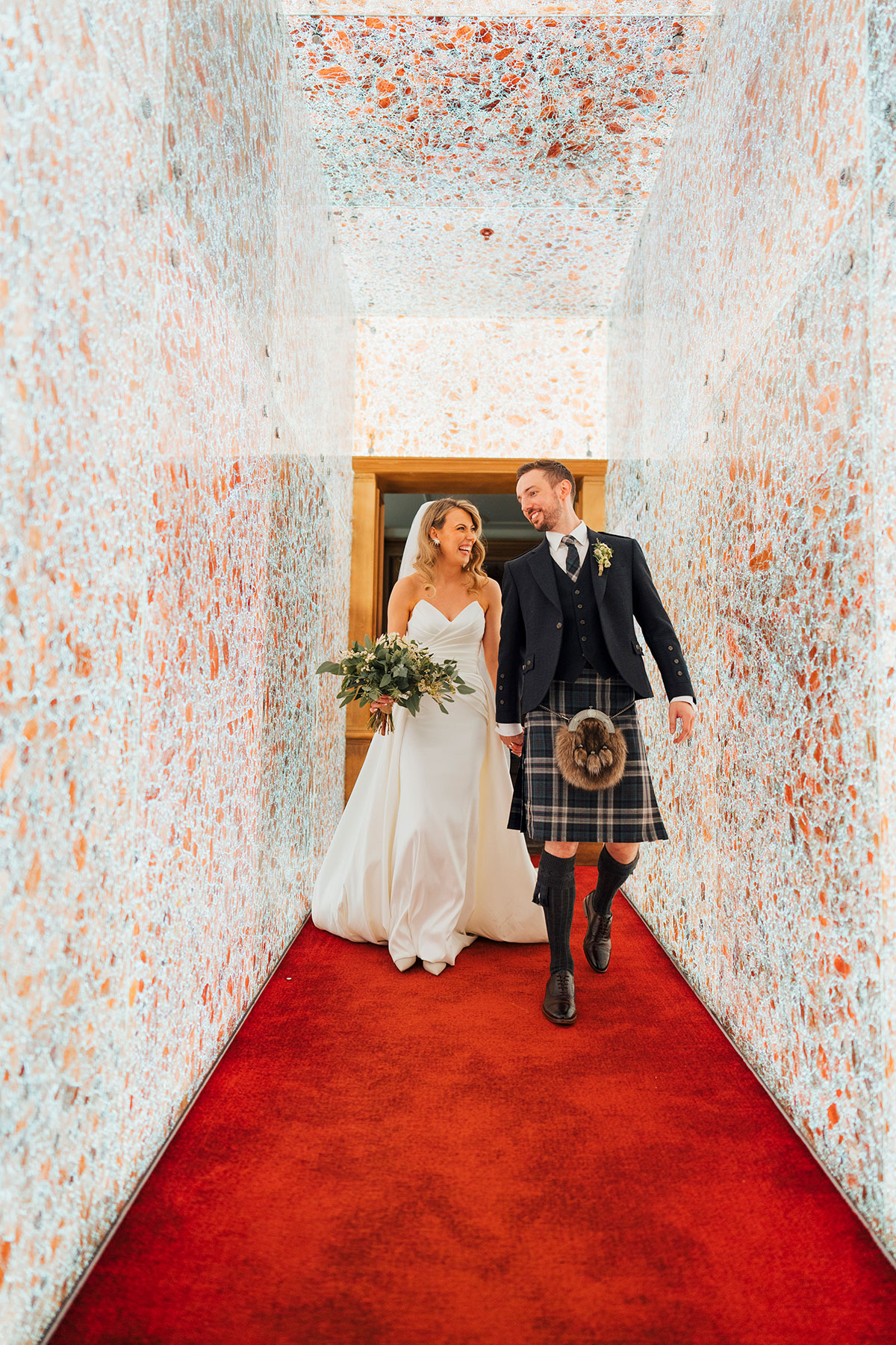 bride and groom walk through corridor with mosaic details at Virgin Hotels Edinburgh