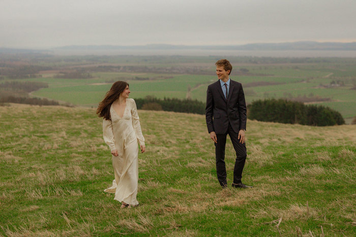 bride and groom smile at one another as they walk through fields at guardswell farm