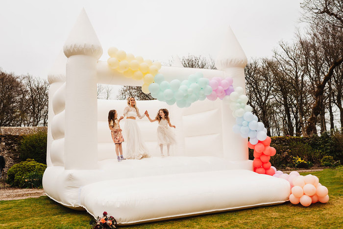 Bride and children jump on white bouncy castle 