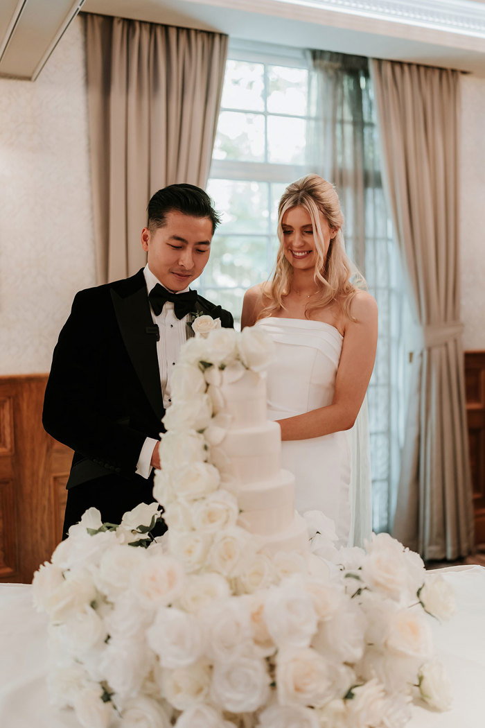 a bride and groom cutting a wedding cake with cascade of white roses