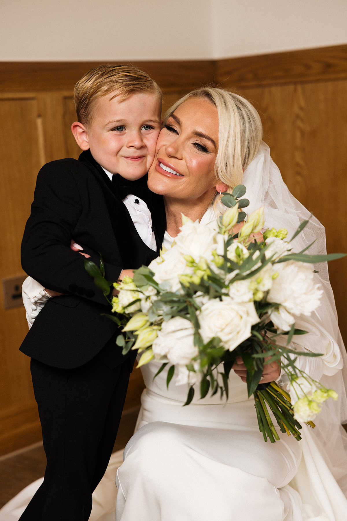 Bride holding a white bouquet and smiling with a young child on the wedding morning