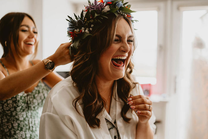 Bride laughs as bridesmaid attaches flower crown to her head