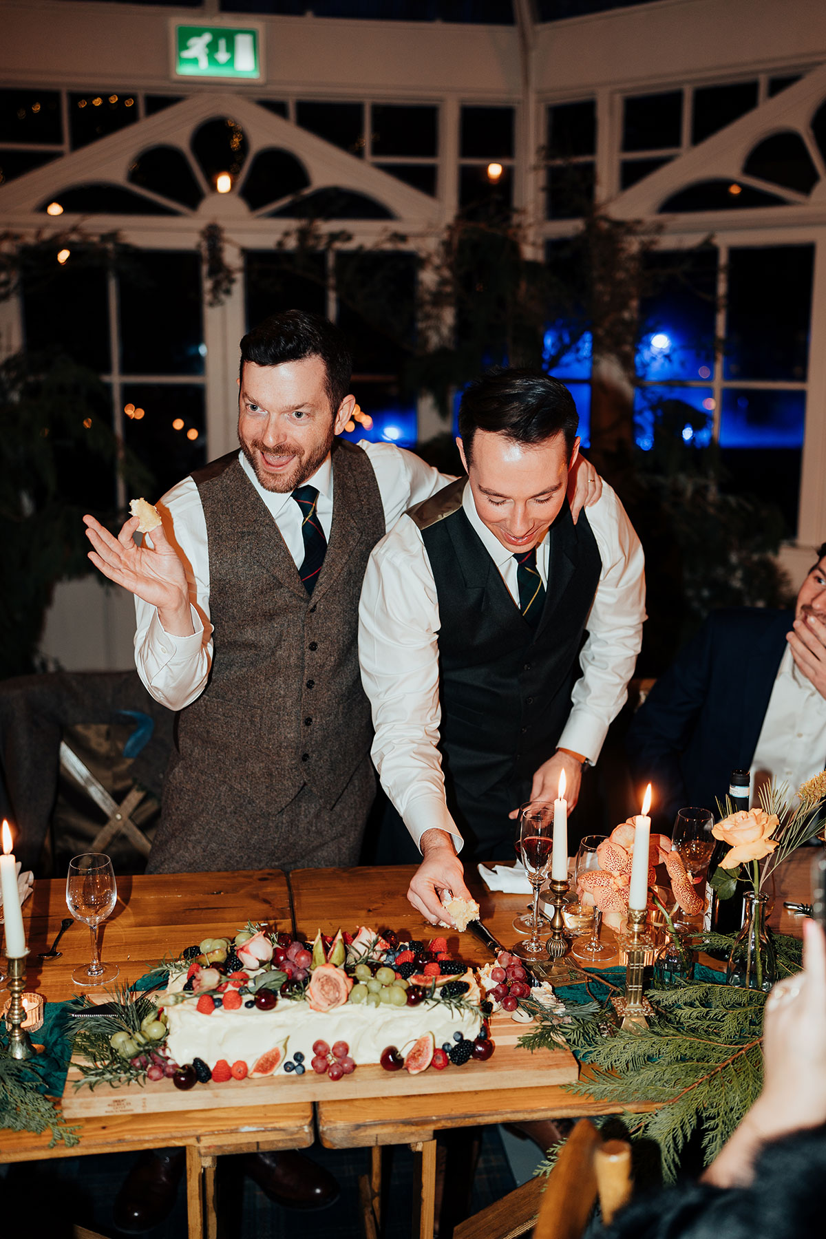 The couple laugh together while cutting their wedding cake during the reception