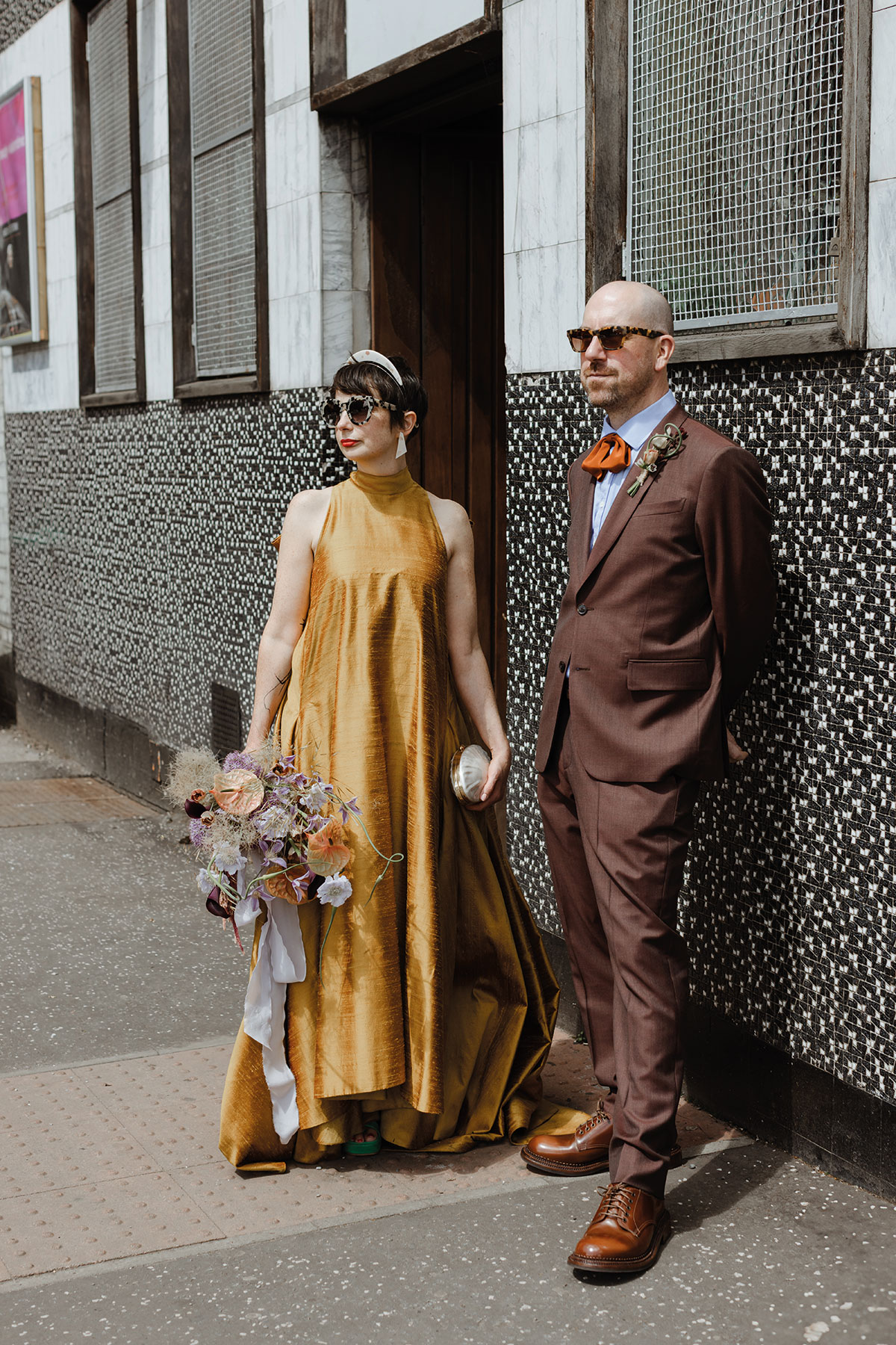 Stylish couple in colourful wedding outfits posing on a Glasgow city street after their modern wedding ceremony
