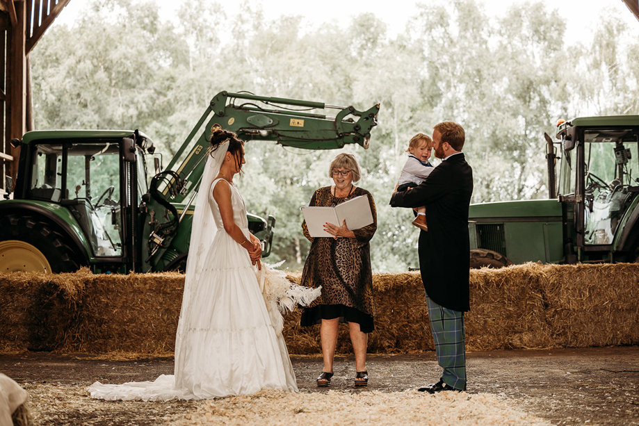 A Wedding Ceremony In A Shed on Boswells Estate With Bride And Groom Standing In Front Of Hay Bales And Green Digger