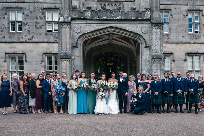 a group of wedding guests lined up and newlywed bride and groom pose outside the facade of Blairquhan Castle
