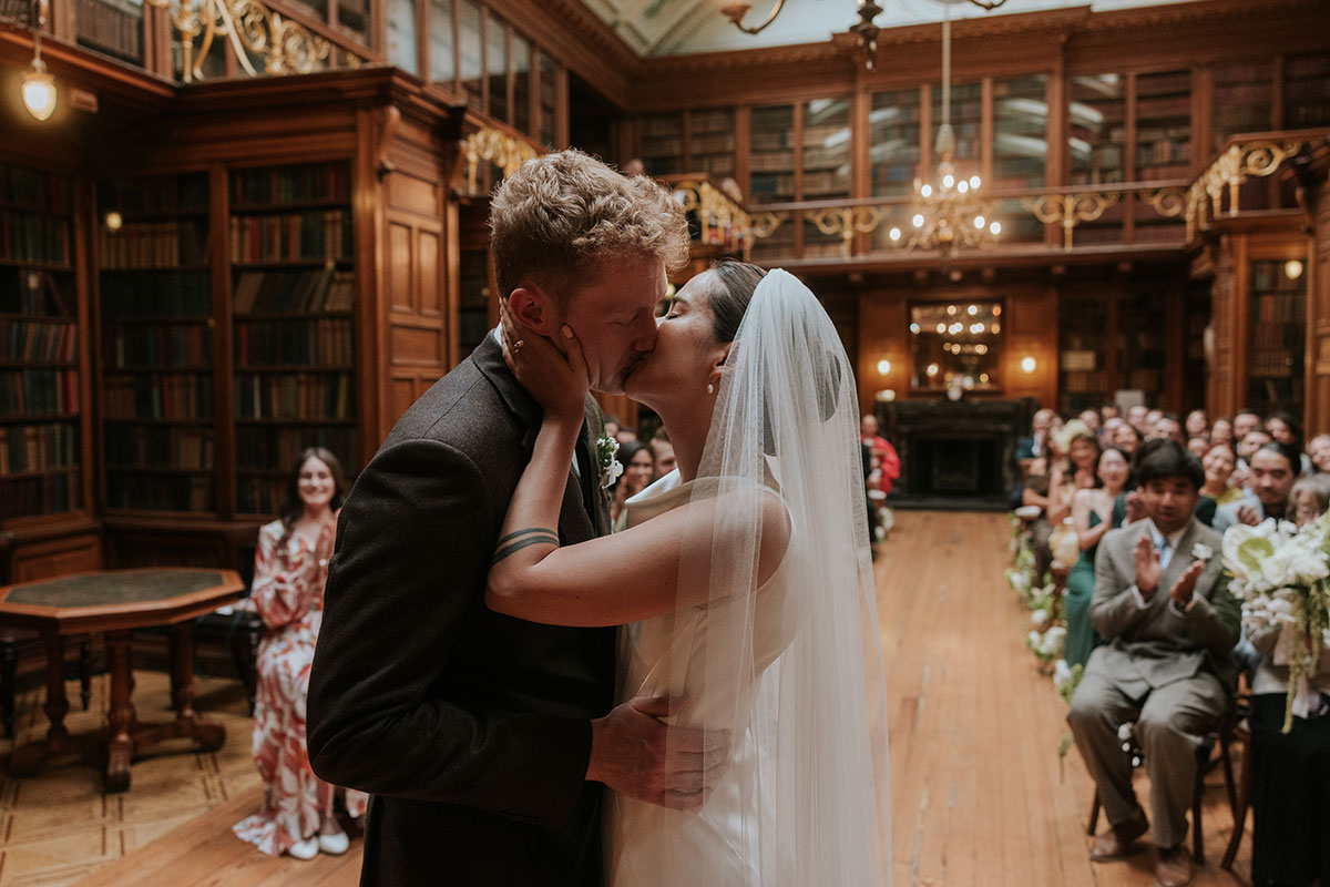 Bride and groom sharing first kiss as newlyweds in front of wedding guests.