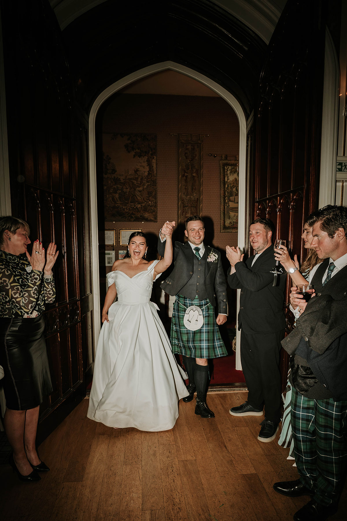 Newlyweds entering Drumtochty Castle reception with guests applauding and groom in traditional kilt