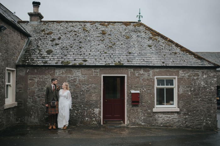 Bride and groom pose against building's stone wall