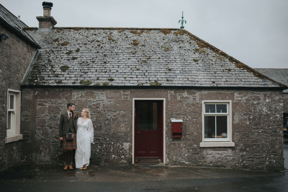 Bride and groom pose against building's stone wall